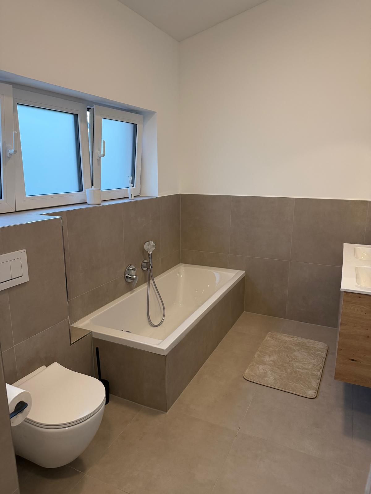 Badezimmer mit eingebauter Badewanne, Wand-WC und grauen Fliesen