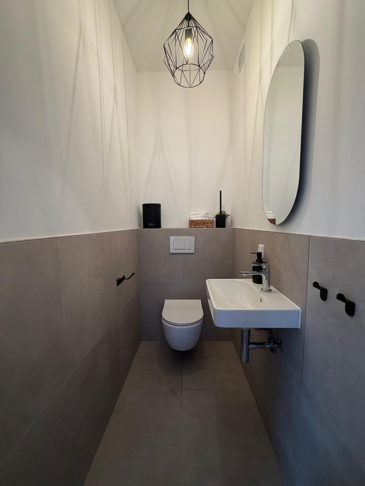 Gäste-WC mit Wand-WC, Waschtisch und ovalem Spiegel