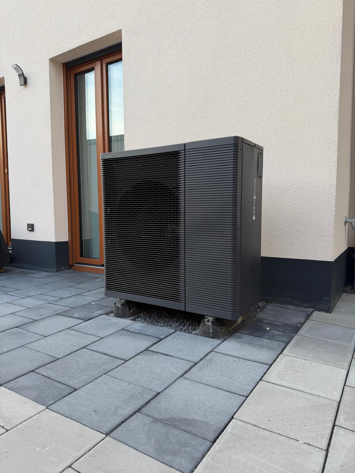 Außeneinheit einer Wärmepumpe vor einer verputzten Hauswand